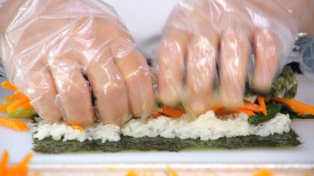 Hands rolling kimbap with carrots