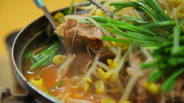 Tongs taking meat out of pork backbone stew with chives and bean sprouts