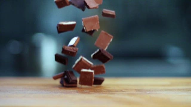 Chocolate pieces artistically falling onto a wooden surface