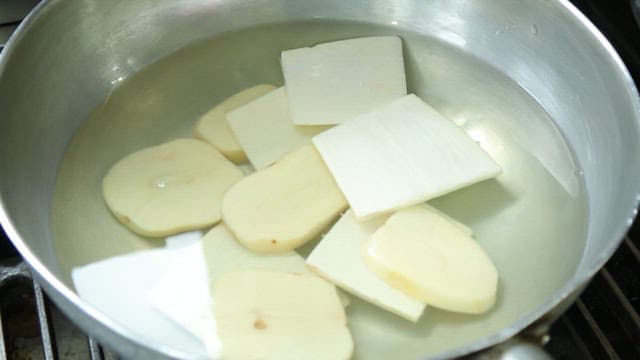 Hand putting vegetables and various fish into a pot