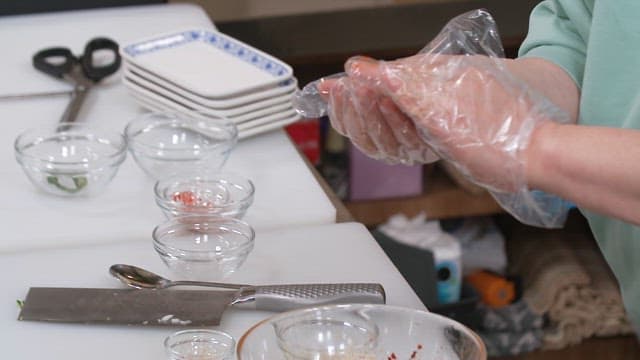 Hands wearing plastic gloves putting seasoned abalone on rice balls