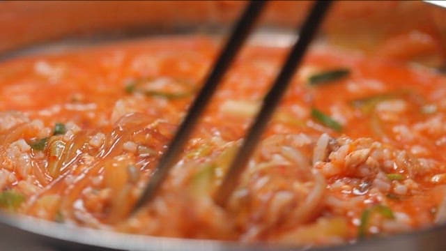 Stir-frying spicy fish porridge with noodles, vegetables, and rice with chopsticks
