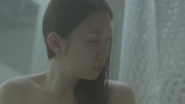 Woman in a bathroom, appears contemplative and slightly melancholic.