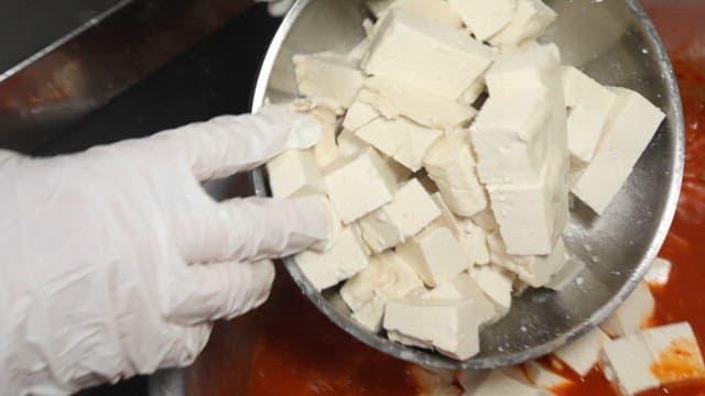 Adding fresh tofu to kimchi stew in a restaurant kitchen