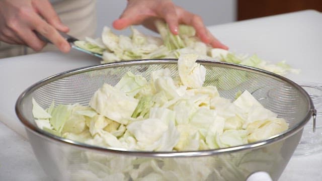 Cutting fresh cabbage with a knife on a cutting board in the kitchen
