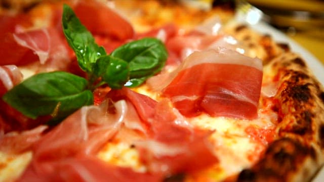 Close-up of a freshly baked pizza with basil and prosciutto