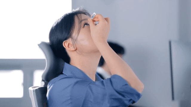 Woman applying eye drops at her desk