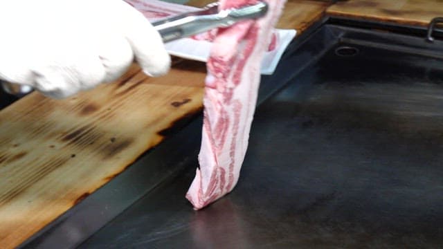 Fresh pork belly being grilled on a hot iron plate