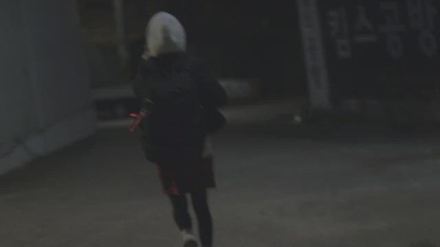 Woman wearing hoodie and jacket running at night while talking on the phone with worried expression