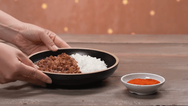 Hands serving a bowl of delicious black bean sauce with rice on a wooden table