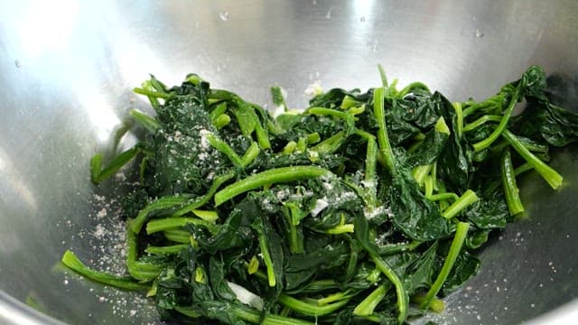 Preparing seasoned spinach in a stainless steel bowl with gloved hands