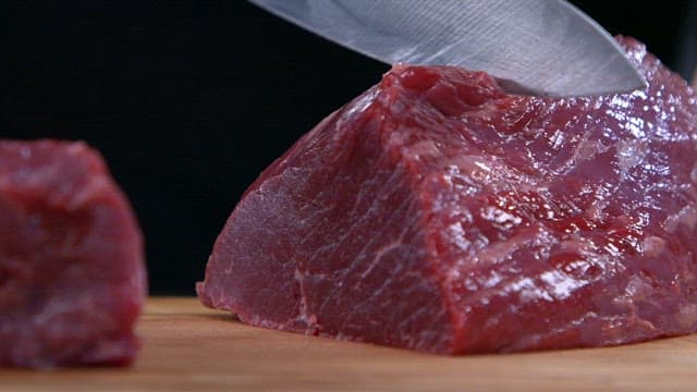 Knife slicing through a piece of raw beef