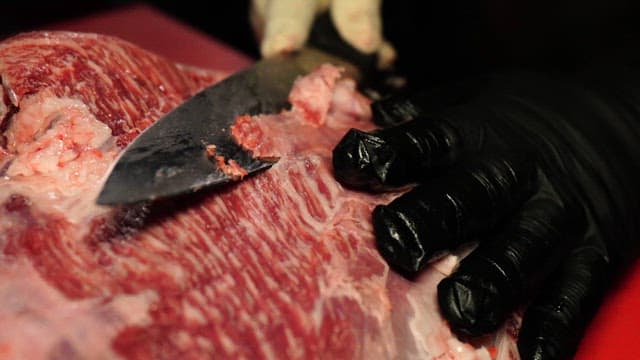 Fresh beef being cut with a knife on a red cutting board