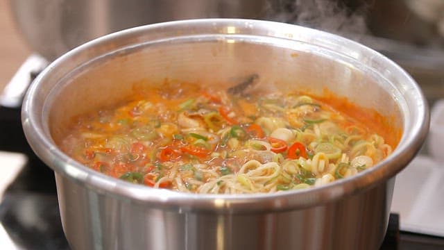 Adding soy sauce to spicy kalguksu noodles boiling in a pot