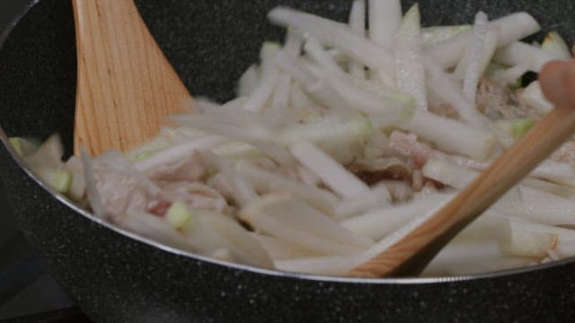 Stir-frying white radish and meat in a black frying pan