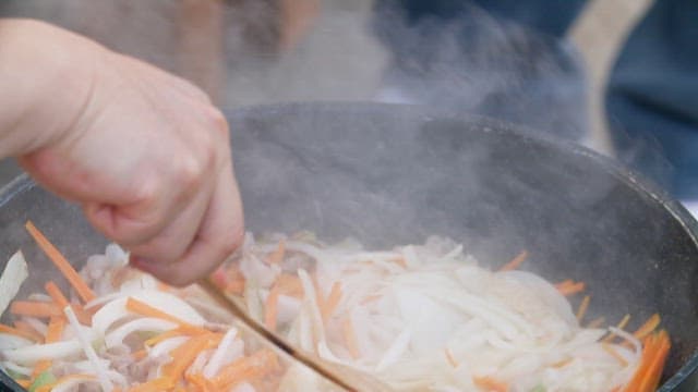 Stir-frying vegetables and meat in frying pan with wooden spatula