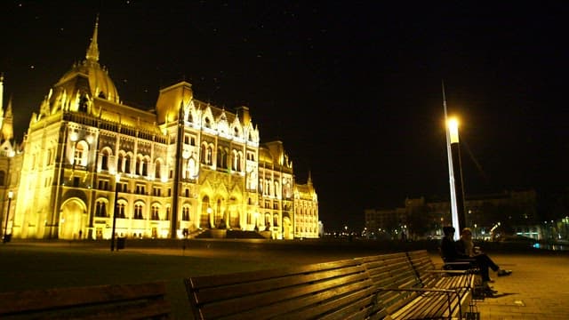 Couple sitting on a bench under a lamppost at night with an illuminated cathedral