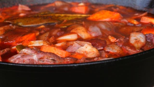 Simmering stew full of vegetables and meat in a black pot