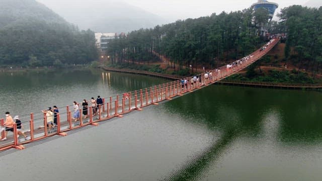 People walking on a suspension bridge over a calm lake
