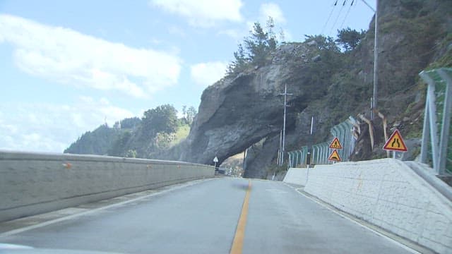 Car Passing Through a Rock Tunnel on a Coastal Road