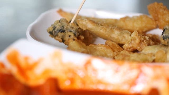 Dipping assorted fried tempura into spicy tteokbokki sauce