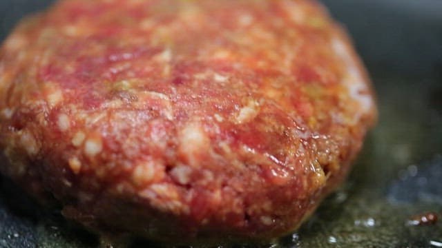 Juicy burger patty sizzling on a pan