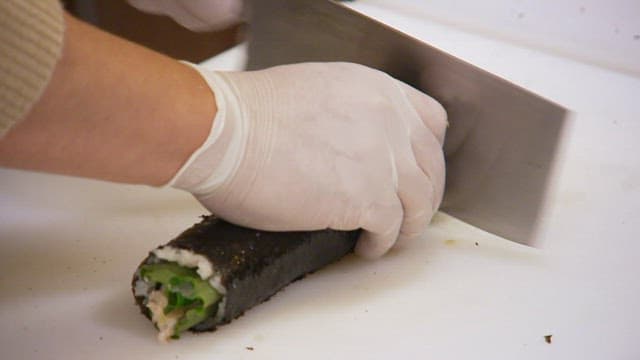 Gloved hand cutting delicious gimbap with a knife on a cutting board
