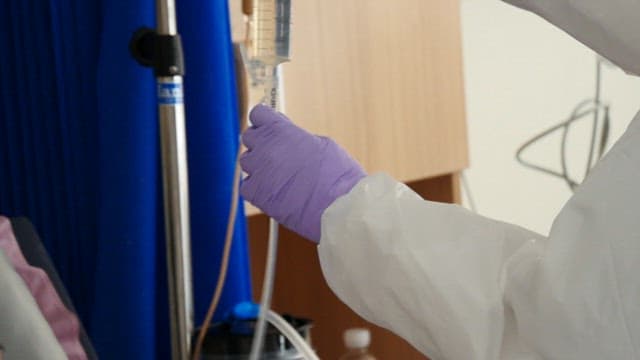 Healthcare worker injecting ringer solution into a tube with a syringe in a hospital room