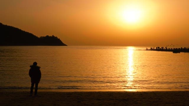Beach sunset with a person in a winter coat watching the horizon