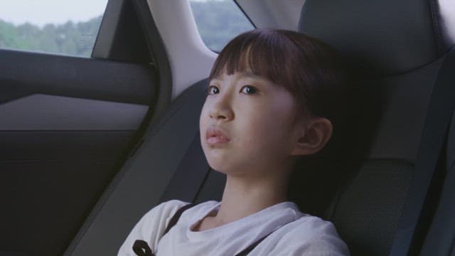 Young girl seated in a car, looking thoughtful.
