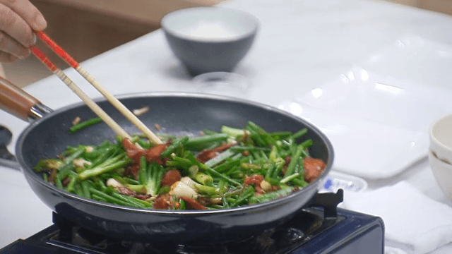 Smoked duck with garlic chives stir-fried in a frying pan on a portable gas stove