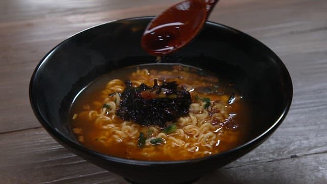 Spicy ramen being served with sauce with spoon