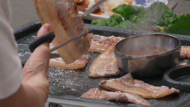Person cutting sizzling pork belly on a grill