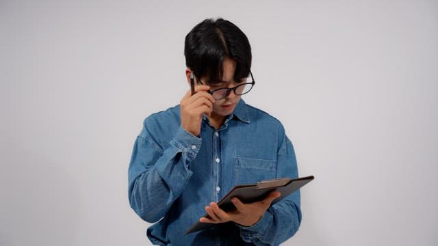 Man wearing glasses writing something on clipboard