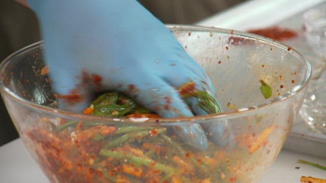 Preparing a spicy vegetable mix with hands in gloves